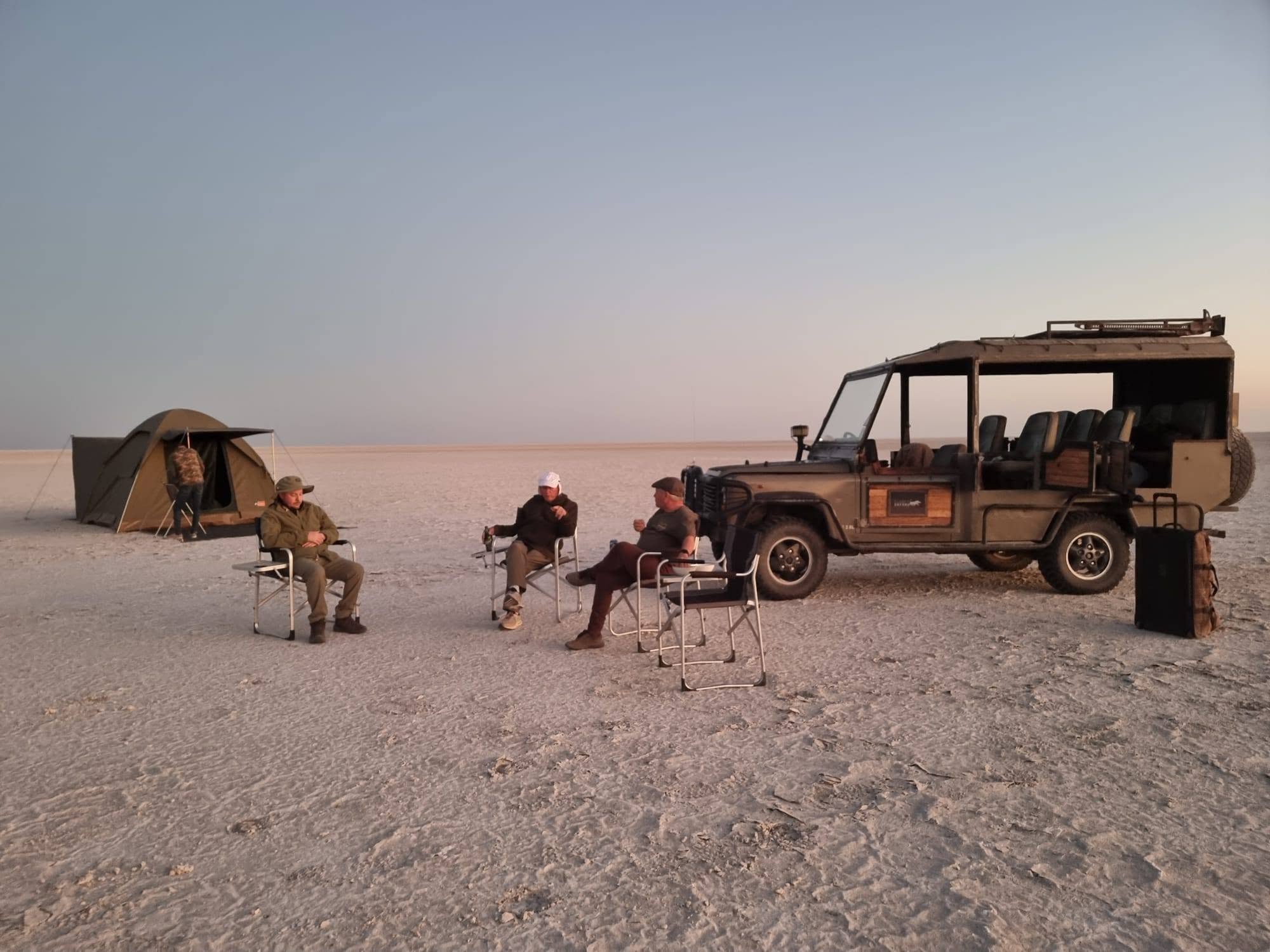 Guests relaxing beside a safari vehicle and tent on Botswana salt pans