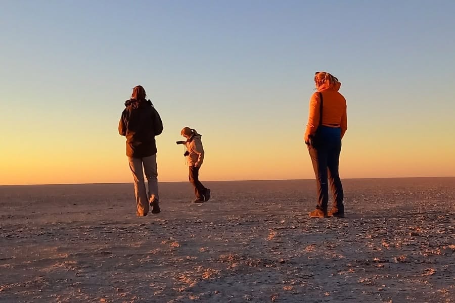 Safari guests walking across Botswana salt pans at sunrise