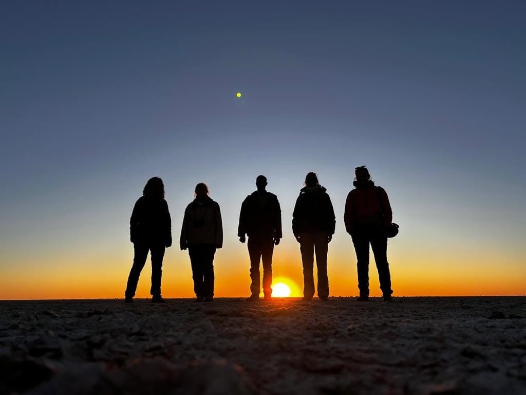 Safari guests silhouetted against a Botswana saltpan sunset